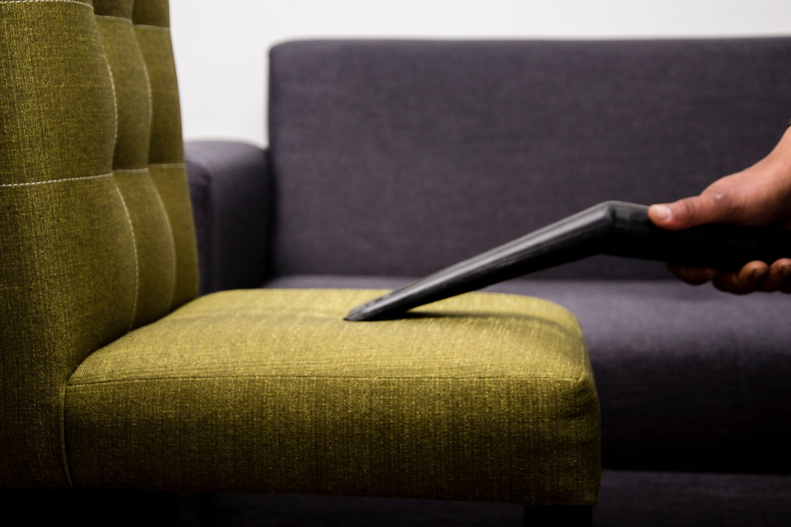 Home Close-up of a person vacuuming a modern sofa chair indoors, highlighting cleaning service.
