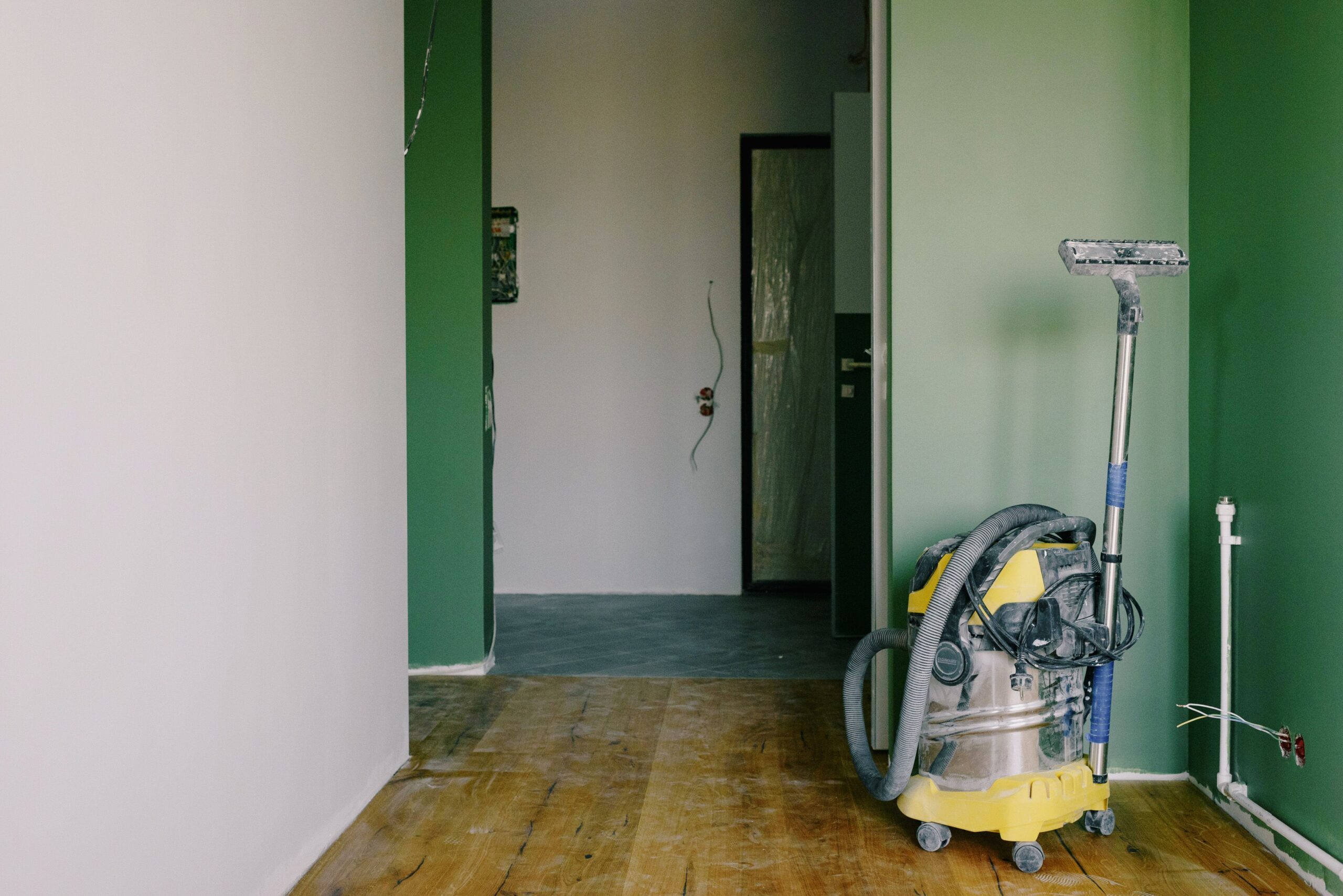 Home Industrial vacuum cleaner placed on dirty parquet in room with green walls and doorway in spacious apartment during repair works
